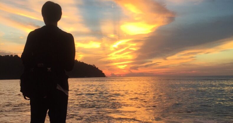 ビーチにいる男の後ろ姿と夕日