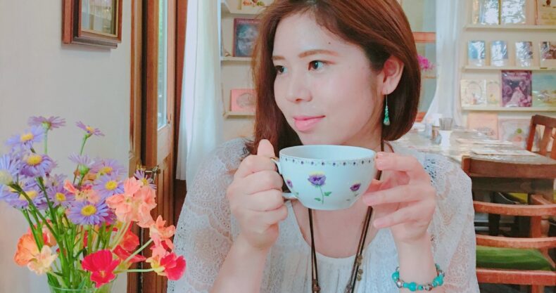 紅茶のカップを持った女と机の上に花瓶と花